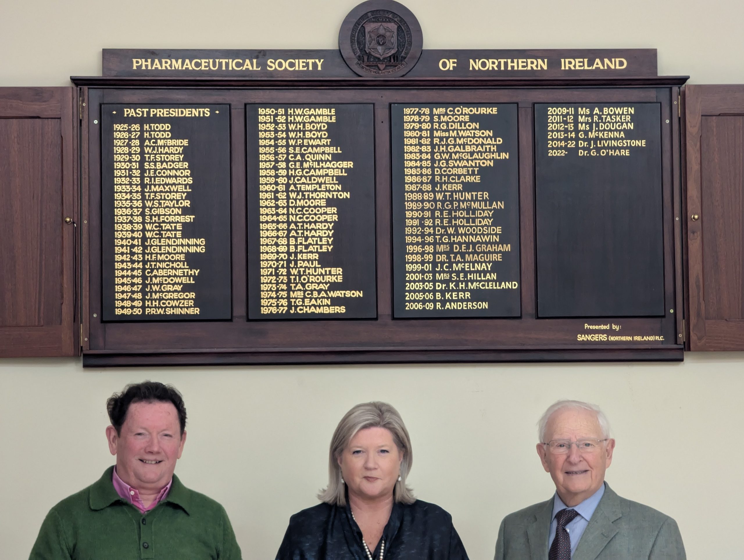 Pharmaceutical Society N I President, Dr Geraldine O'Hare (centre), joined by past Presidents Dr Terry Maguire (left) and Mr Tom Eakin (right) standing below the board that lists all past presidents.